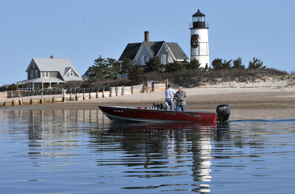 two men fishing on a boat in cape cod with a lighthouse in the background